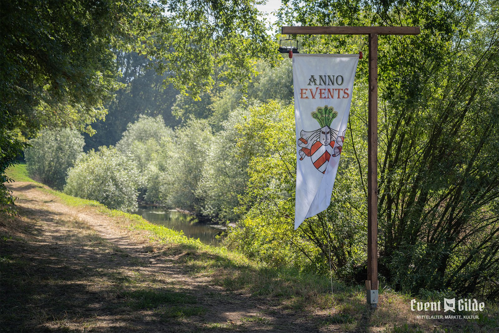 Banner von Anno Events am schattigen Fußweg entlang der Ems zum Festgelände in Telgte