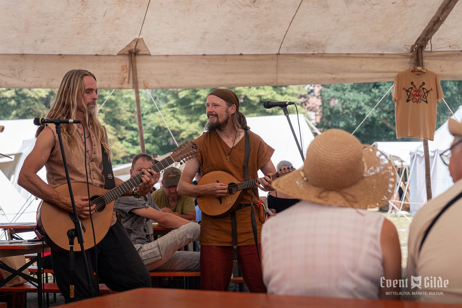 Zwei Spielleute von Sonor Teutonicus singen mit Gitarre und Cister unter dem großen Zelt vor sitzenden Gästen