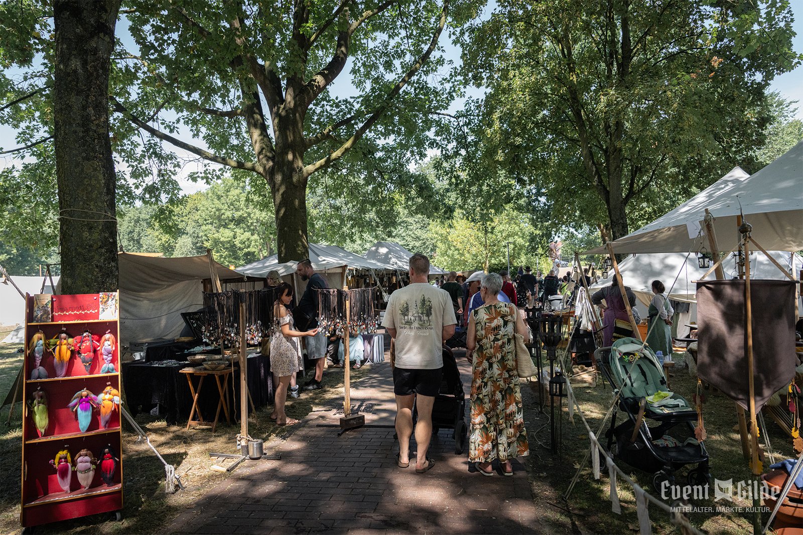 Gäste bummeln zwischen Marktständen im Schatten der Baumkronen beim Mittelaltermarkt in Telgte