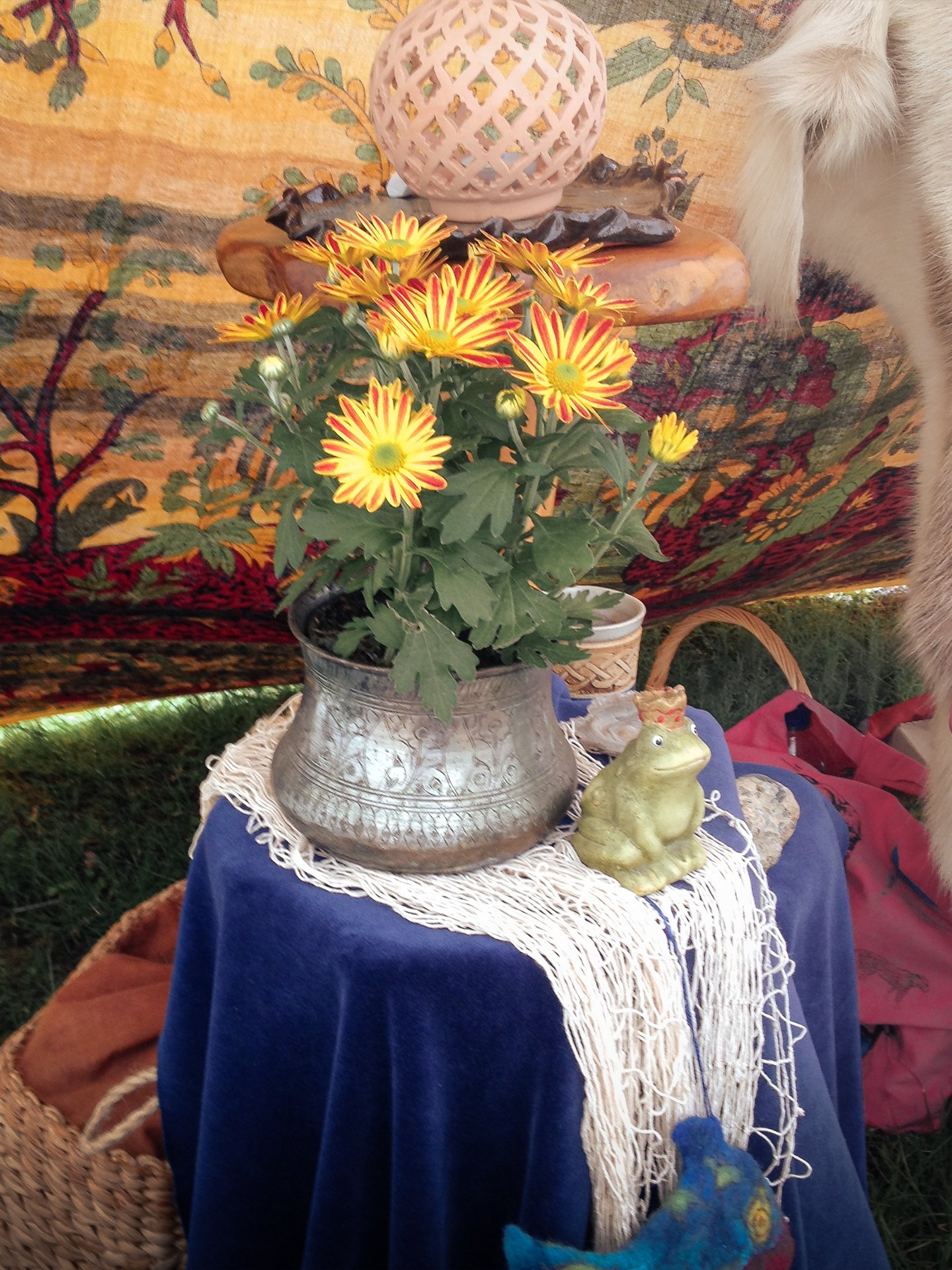 Requisiten aus der Schatztruhe im Märchenzelt, ein getöpferter Froschkönig mit Krone neben Blumen auf blauem Samt