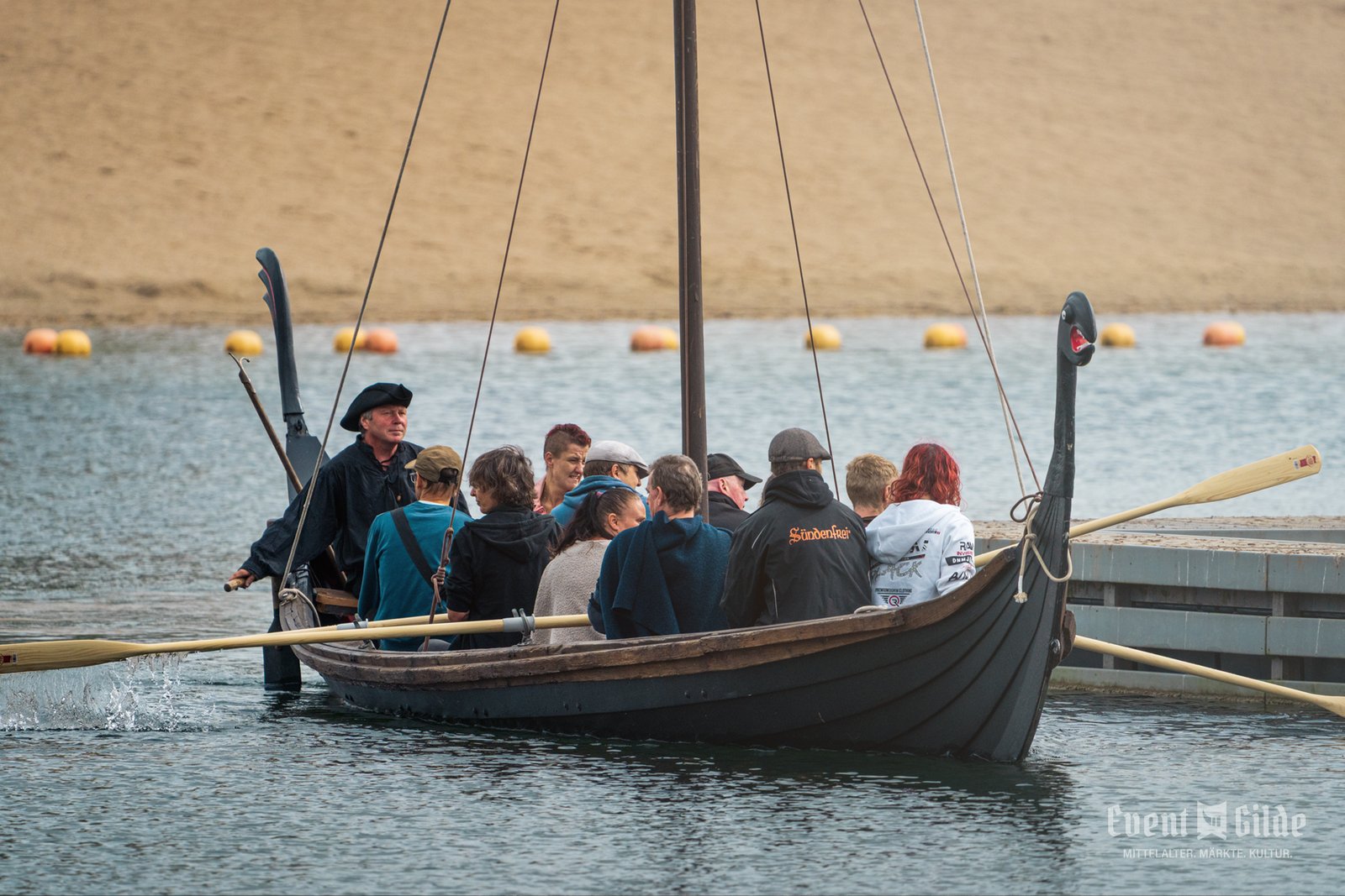 Wikingerschiff mit Drachenkopf am Bug und einer Gruppe rudernder Gäste an Bord auf der Xantener Südsee